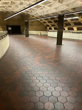 A picture of a metro station pathway. There are wayfinding structures slightly off center to the right and left, with the structure to the right being closer than the structure to the left. There are multiple half walls with railings on top of them in the image, with one to the left, one in the center of the background, and one to the right running from the background towards the foreground.